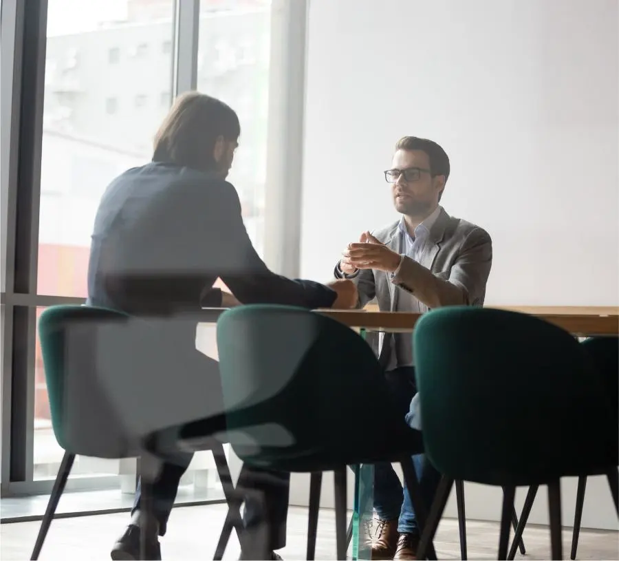 Dos hombres conversan sentados a la mesa de un despacho.