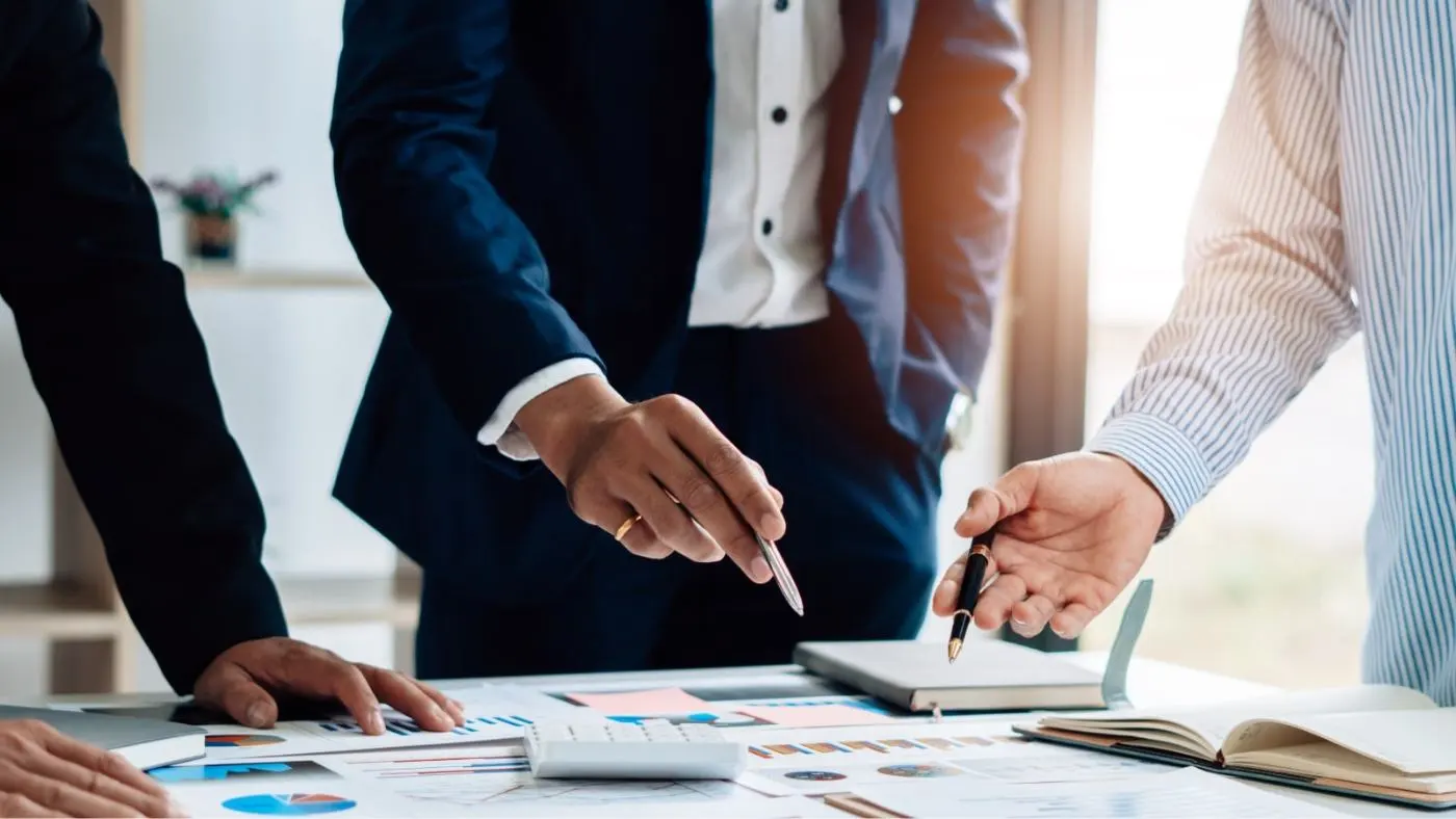 Tres hombres de negocios discuten sobre varios gráficos de colores extendidos ante ellos.