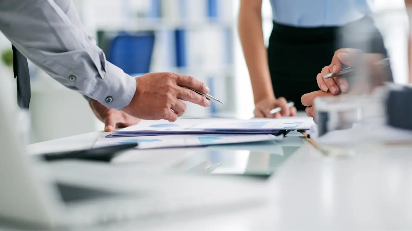 Tres personas discuten sobre unos documentos que tienen sobre la mesa.